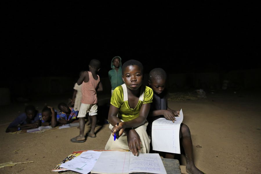 Des enfants étudient le soir près d'une lampe solaire dans la maison du chef de village Mbil Ayaada. 