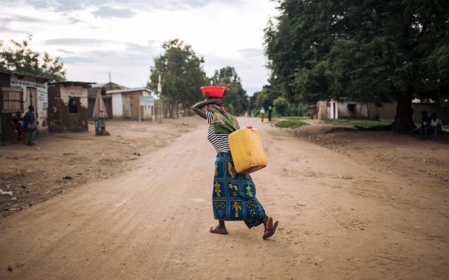 Rizini Furaha carries a water jerrican at dusk in Malinde, DRC.