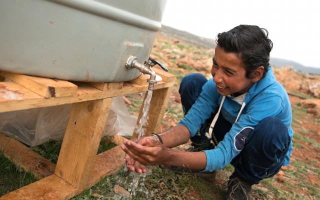 A resident of Btedai ITS (Informal tented settlement) washes his hands with water from an Oxfam provided water tank.