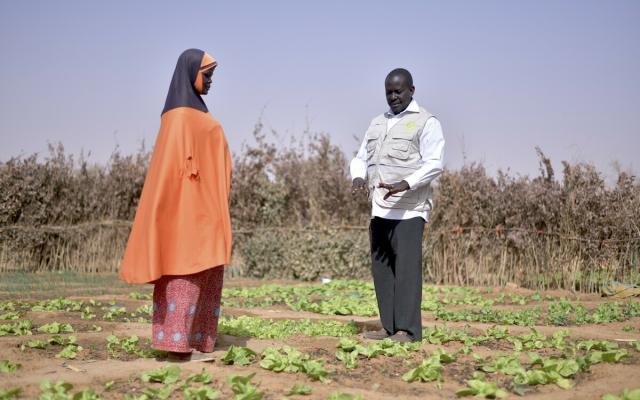 Mariama (left) stands with Hassane Harouna (right), Oxfam Base Manager in Ouallam, Niger, on the plot of land she farms to survive.