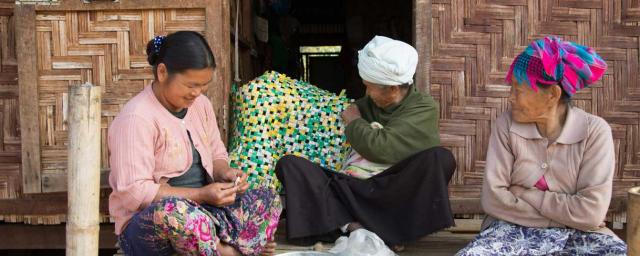 Hpa na Nam, de 42 años, con su madre y su abuela en el porche de su refugio. Haciendo esteras con envoltorios de café y té, como le enseñó su abuela. Crédito: Pye Aye Nyein / Oxfam Novib