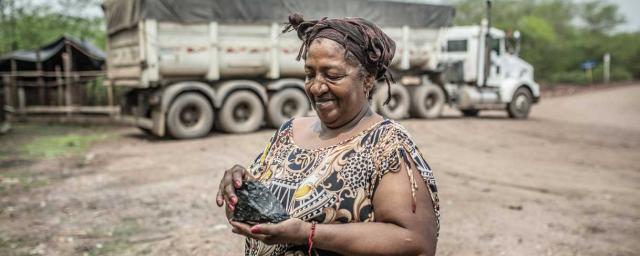 Eneida Díaz avec un morceau de charbon dans la main à côté d'un camion de transport. La nouvelle mine a pollué l'air et le sol. Elle a également détourné, contaminé et asséché des sources d'eau. Des communautés ont perdu leurs moyens de subsistance et ont été déplacés. Crédit : Pablo Tosco / Oxfam Intermón