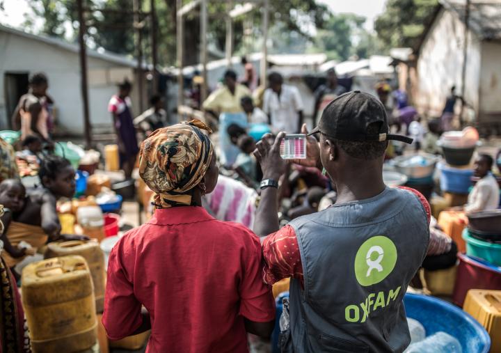 Un técnico de agua y saneamiento de Oxfam junto a un grupo de mujeres recogiendo agua en un punto de distribución construido por Oxfam en el campo de desplazados de Mukassa en Bangui. Credito: Pablo Tosco/Oxfam