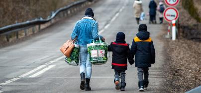 A woman with two children and carrying bags walk on a street to leave Ukraine.