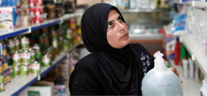 A woman holding a gallon of shampoo in a grocery store.