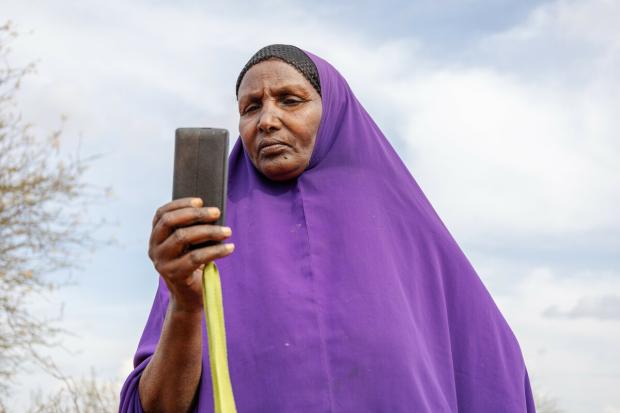 Ebla Hussein Ahmed reading a message from her mobile phone at her home in Elben, Wajir County, Kenya. She receives her monthly cash payment notification via her phone.